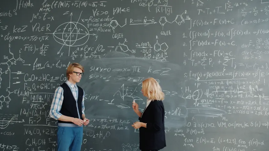 Two educators discussing math and chemical formulas on a blackboard.