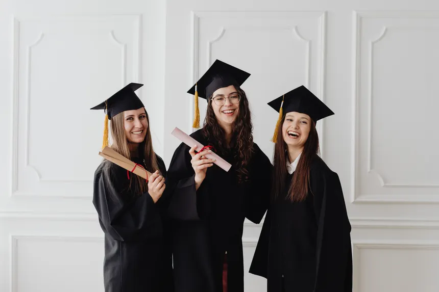Three happy female graduates in caps and gowns holding diplomas and celebrating their achievement.