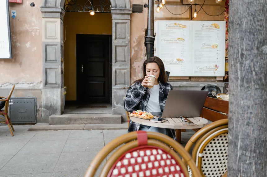 A woman sipping coffee while working on her laptop at an outdoor cafe terrace. Urban lifestyle scene.
