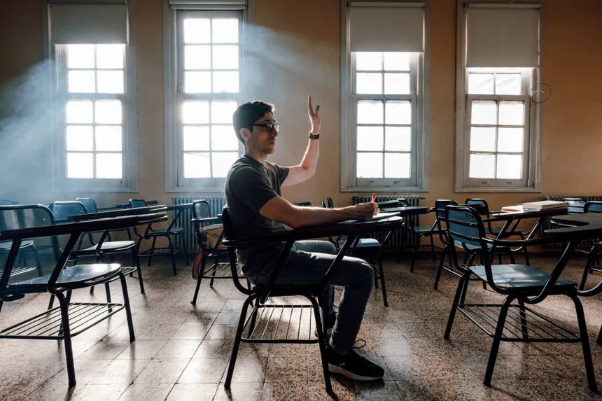 A student raises hand in a university classroom, Buenos Aires, featuring warm light and empty desks.