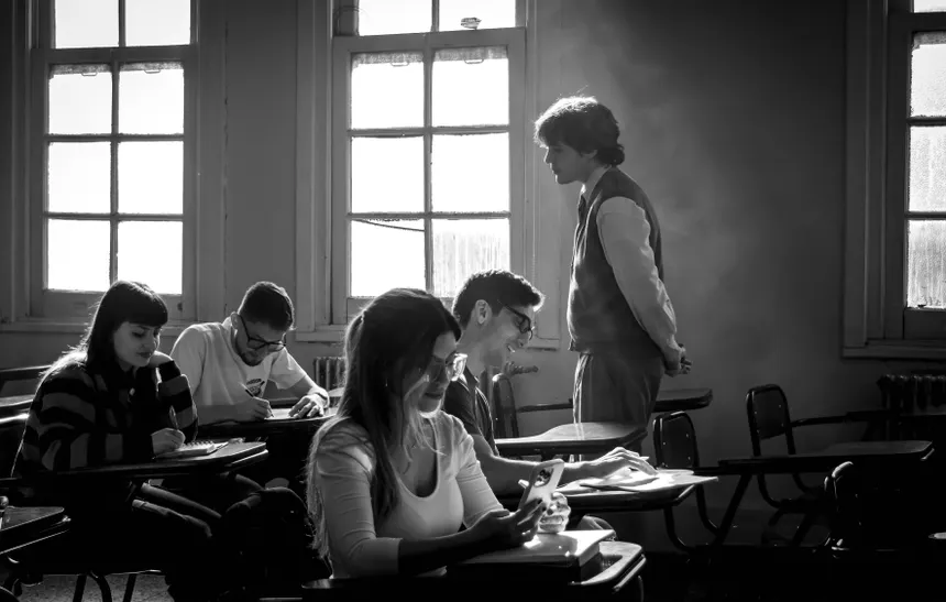 Black and white image of students studying in a classroom with a teacher present.
