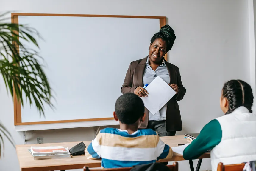 Back view of diverse school children communicating with African American woman against whiteboard in classroom