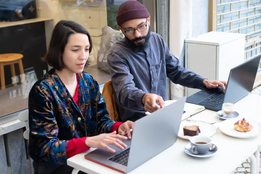 Two adults working on laptops in a cozy café, enjoying coffee and pastries. Perfect for remote work themes.