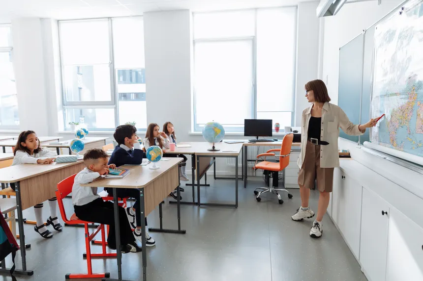 Children in a classroom learning about geography with a teacher using a map.
