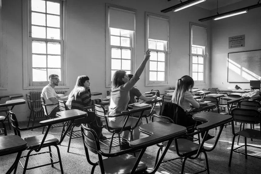 Students in a classroom during a lesson, with one raising hand.